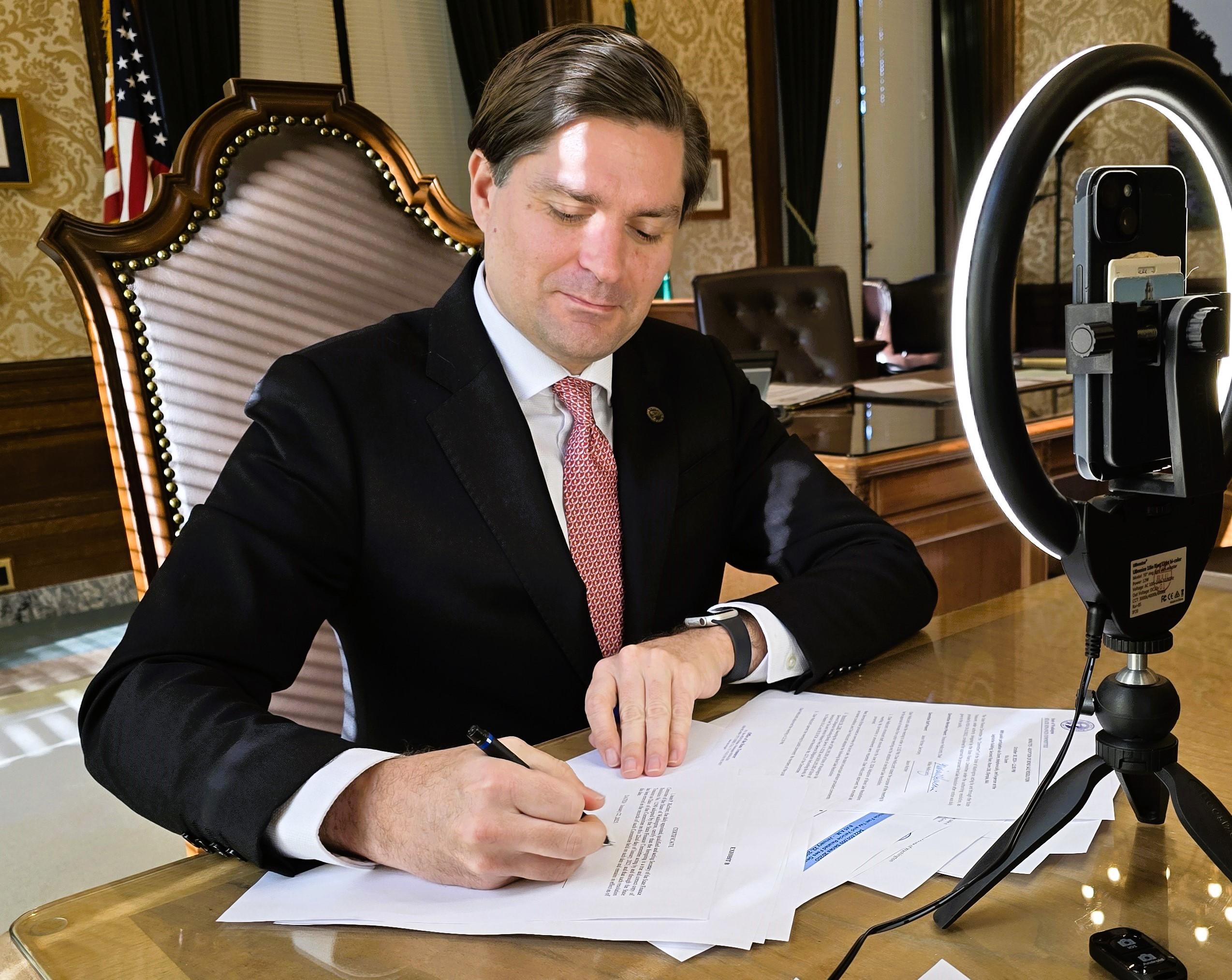 Treasurer Mike Pellicciotti seated at a desk signing WA bond sale documents.jpg