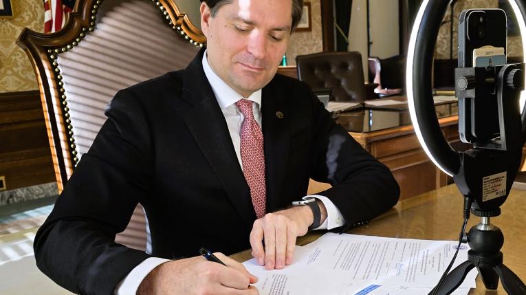 Treasurer Mike Pellicciotti seated at a desk signing WA bond sale documents.jpg